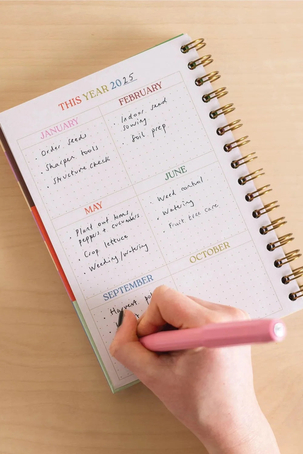 Person writing in a planner with a pink pen on a wooden surface