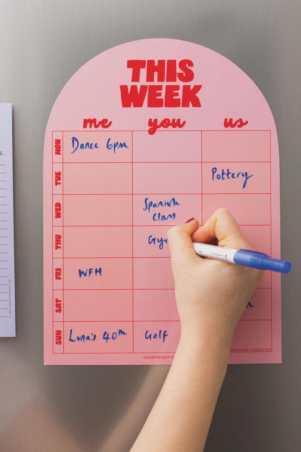 Pink weekly planner with a hand writing on it against a gray background
