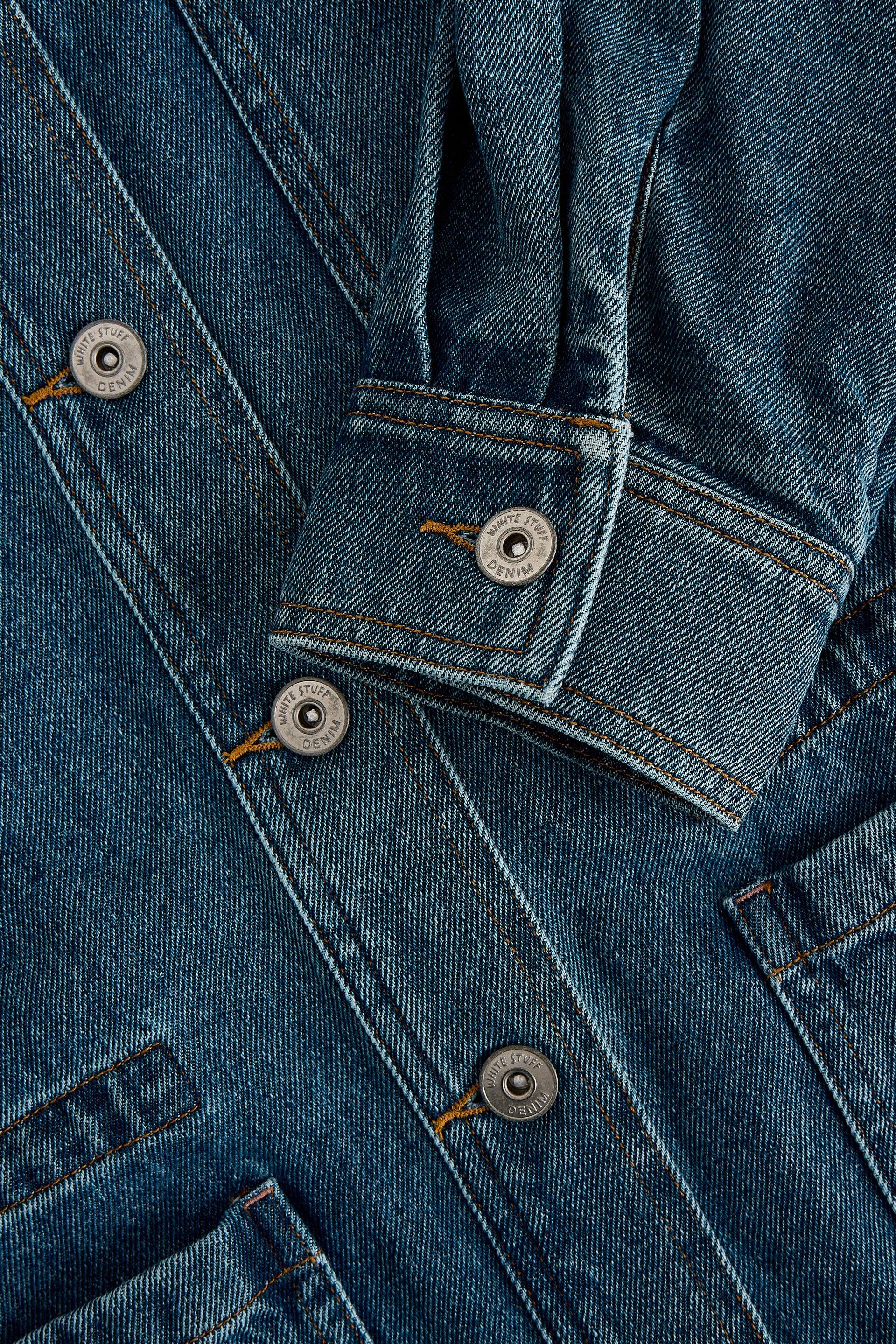 Close-up of a blue organic cotton denim jacket with buttons and stitching details.