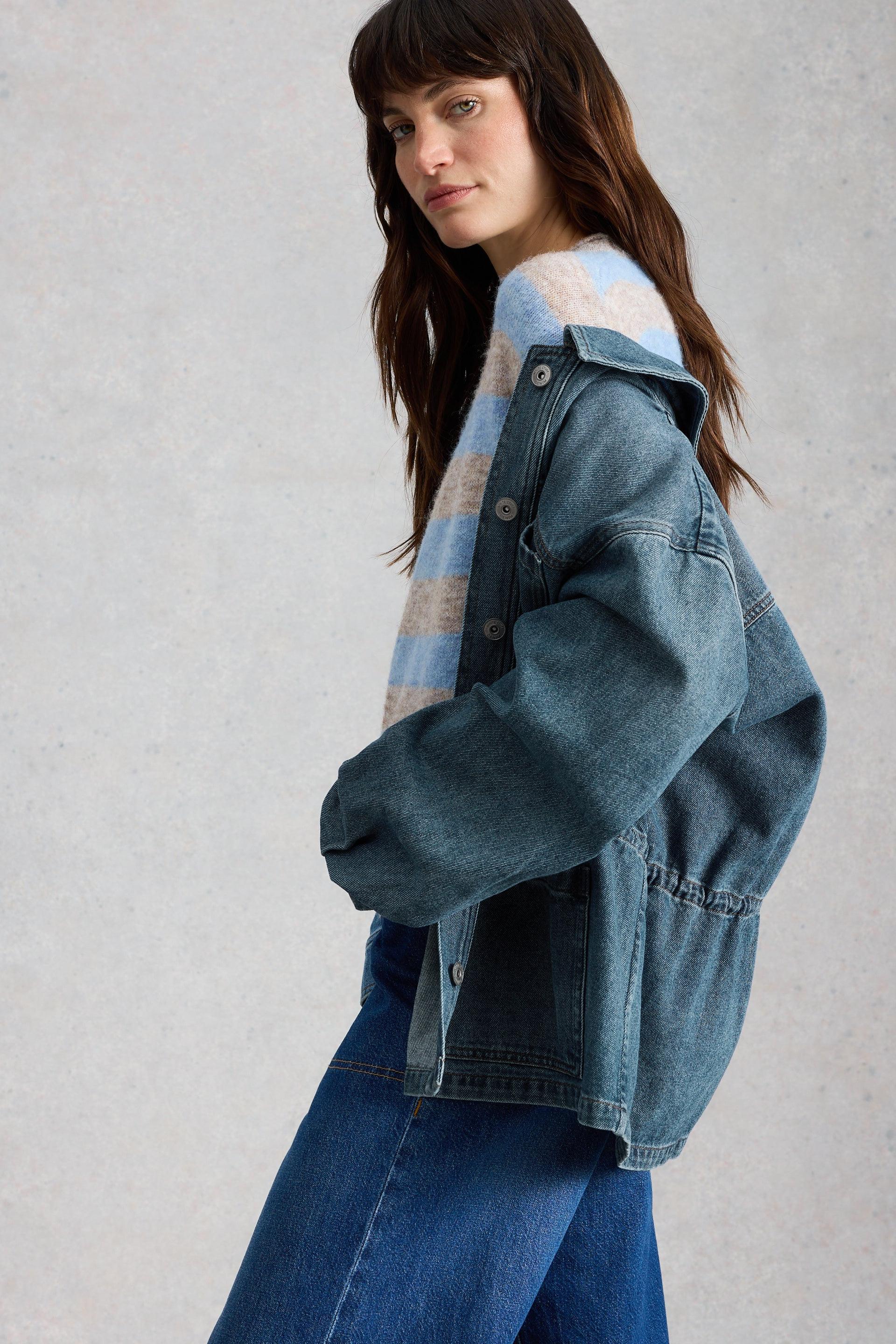 Woman wearing a White Stuff denim jacket over a patterned knit top against a plain background