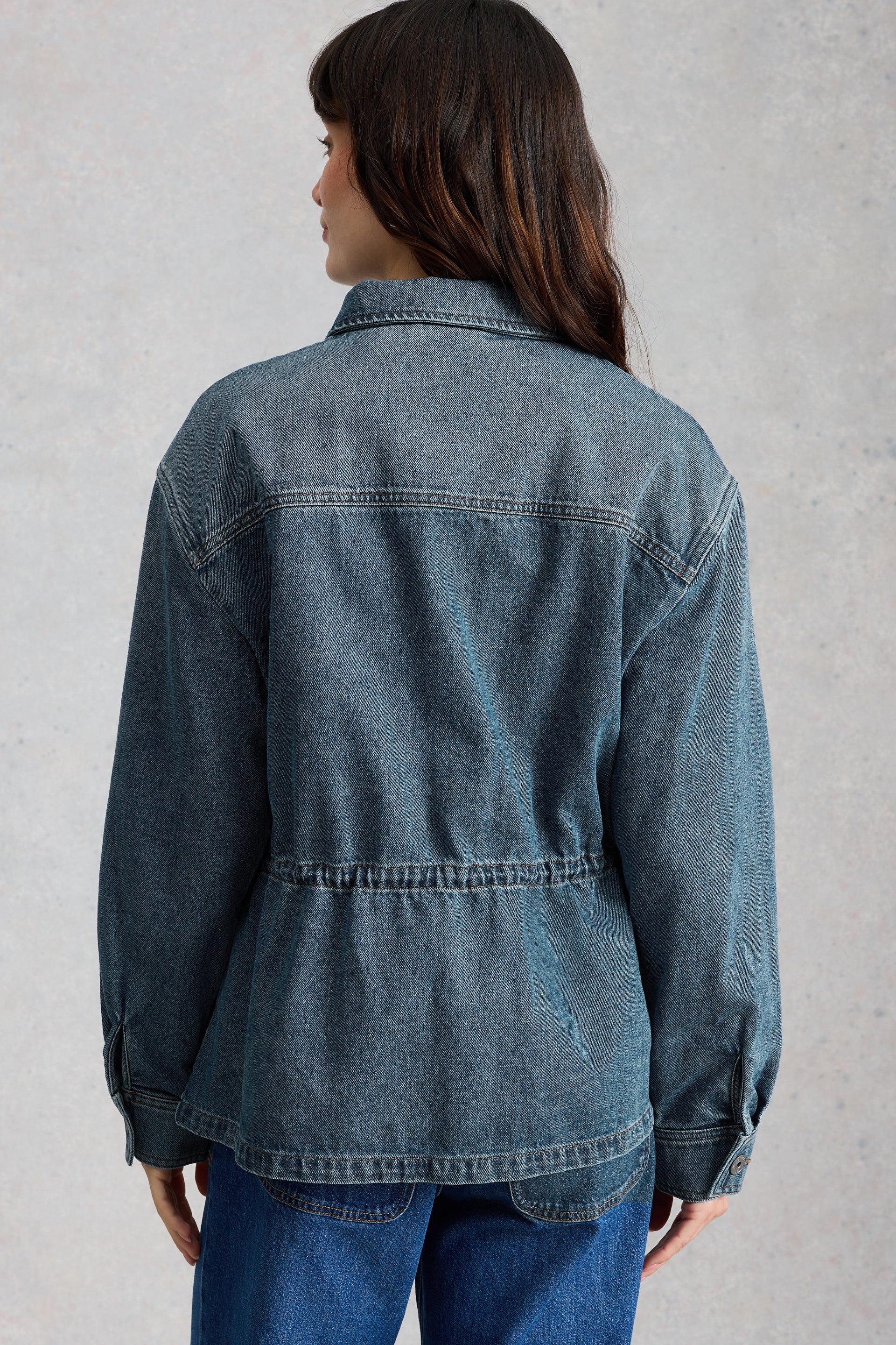 Person wearing a blue utility style denim jacket against a gray background