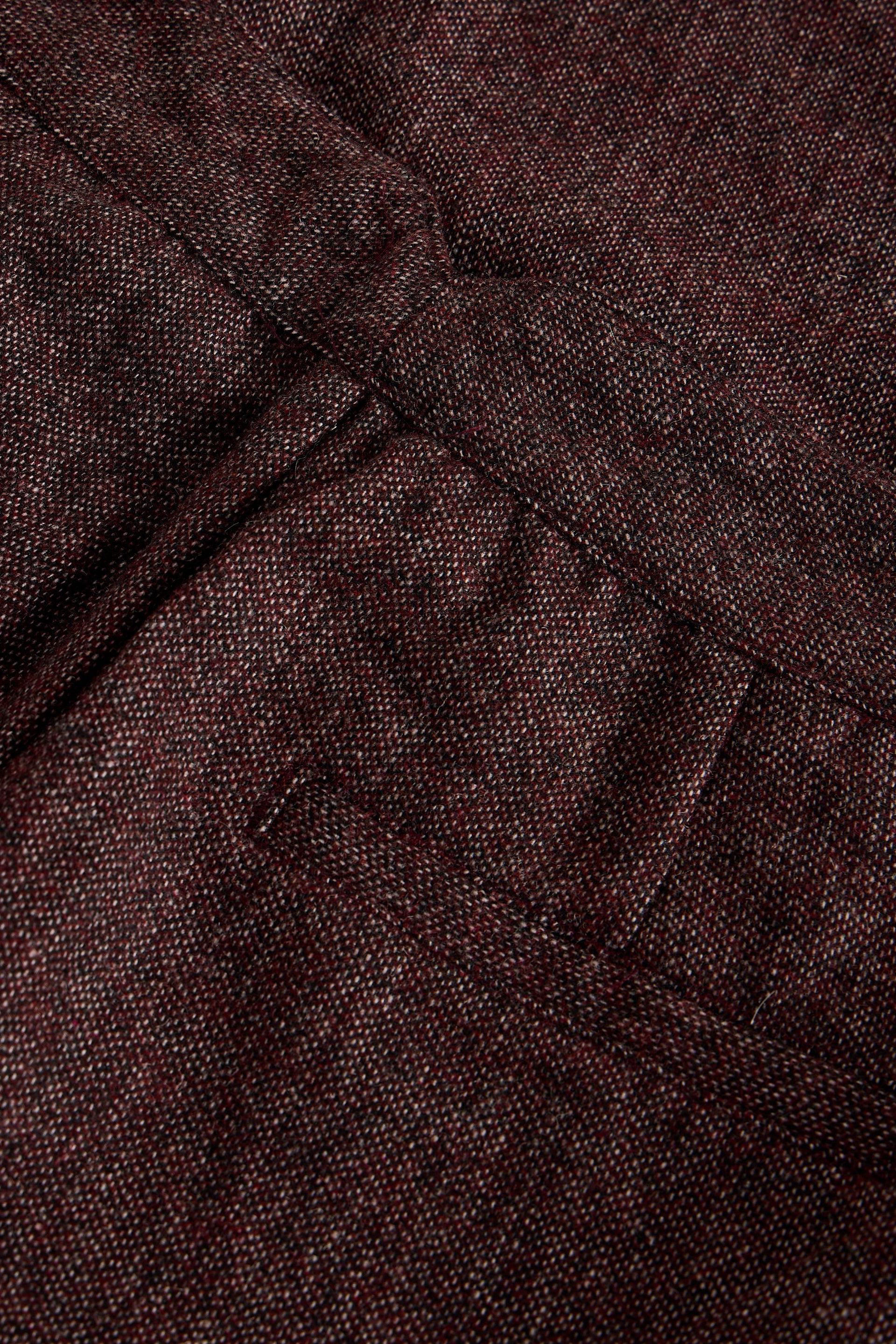 A close-up of dark burgundy textured fabric with visible weave detail and a stitched pocket seam.