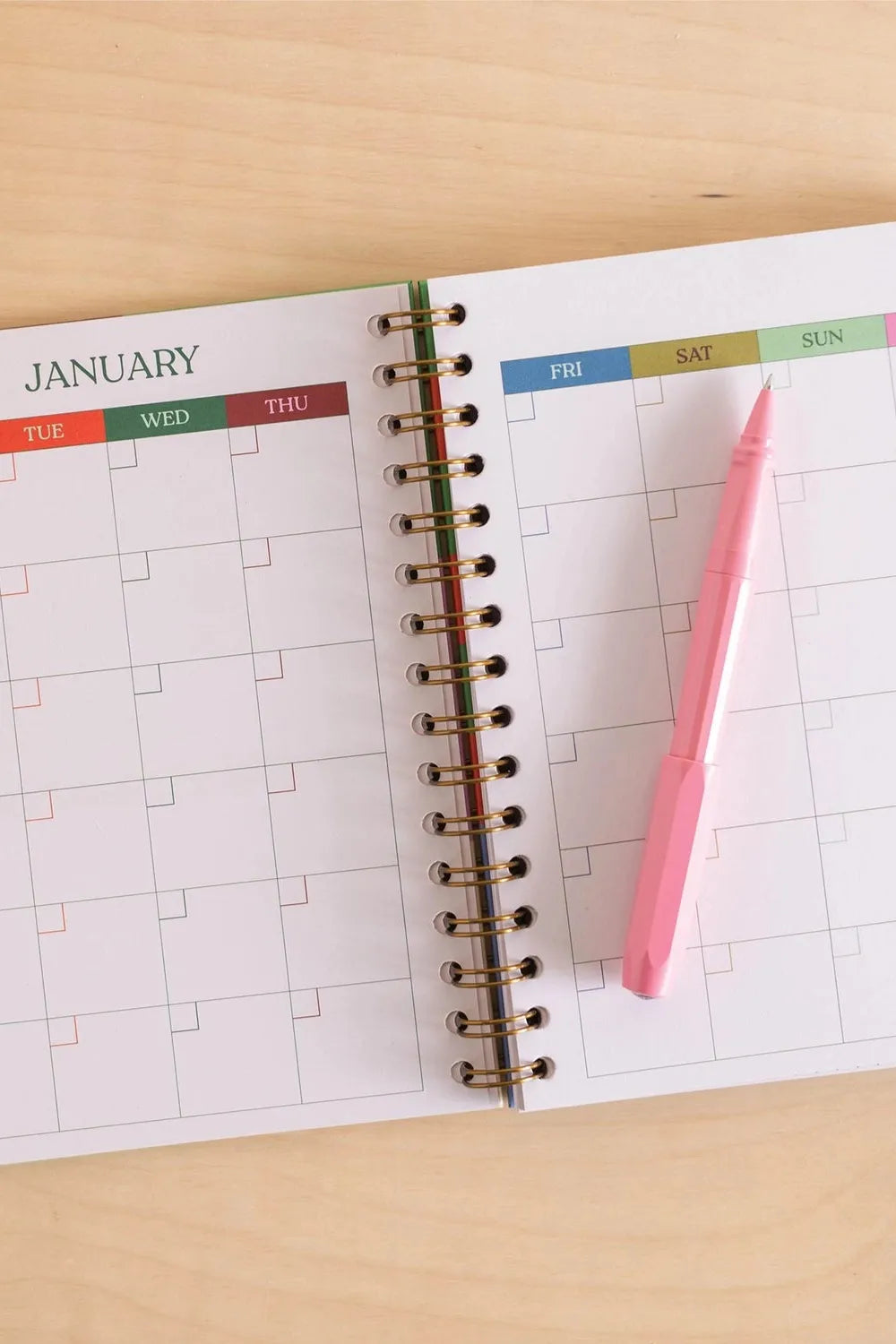 Open planner with January calendar page and pink pen on a wooden surface