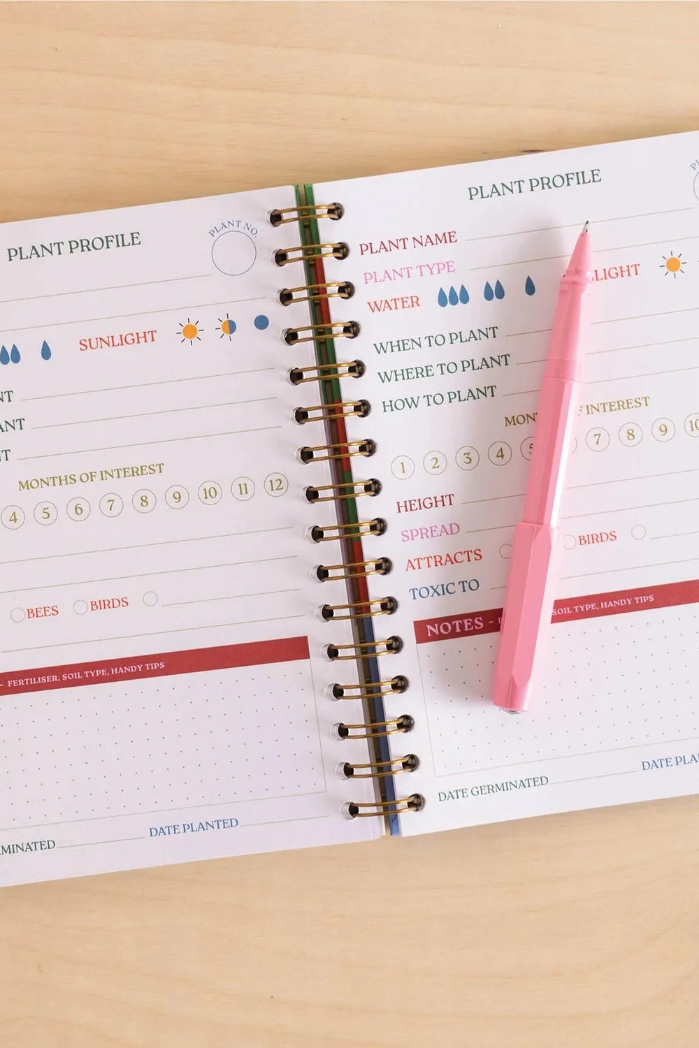 Open planner with plant profile section and pink pen on a wooden surface