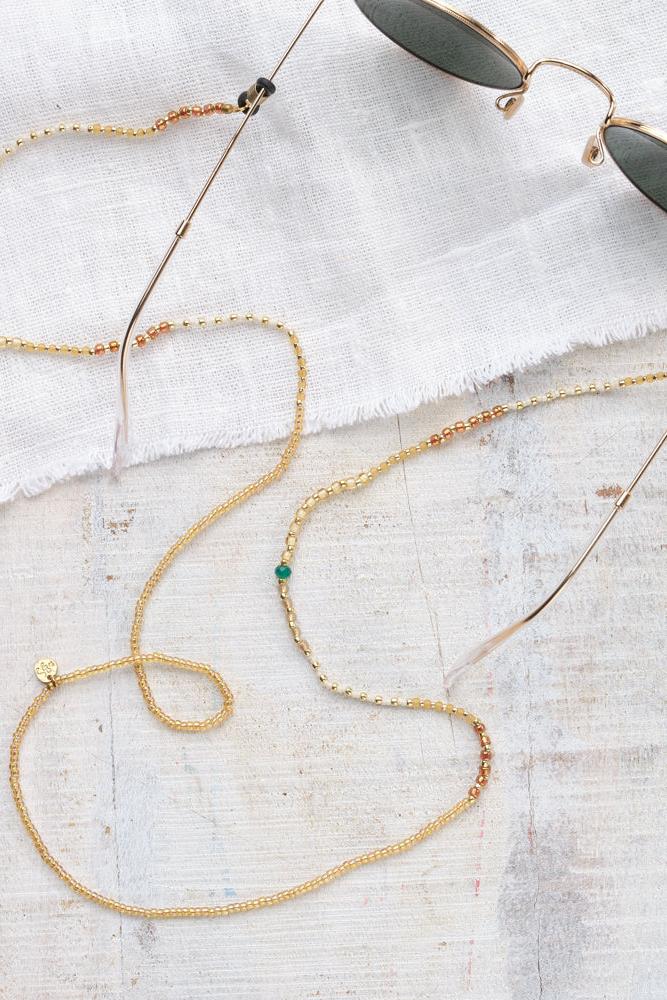 Gold glasses cord with a small green gemstone on a light gray surface