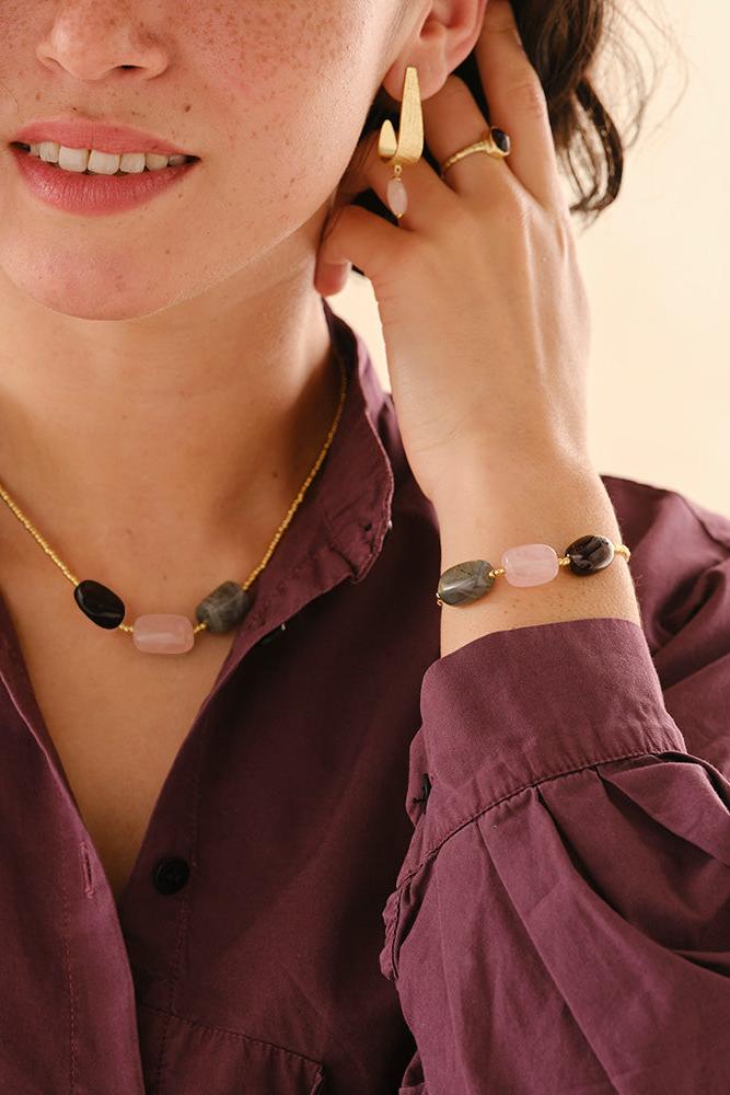 Close-up of a person wearing gold jewelry with gemstones, including earrings and a bracelet.