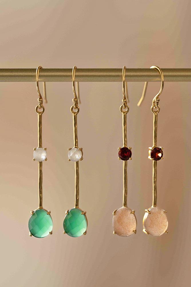Two pairs of gold earrings with various gemstones on a beige background