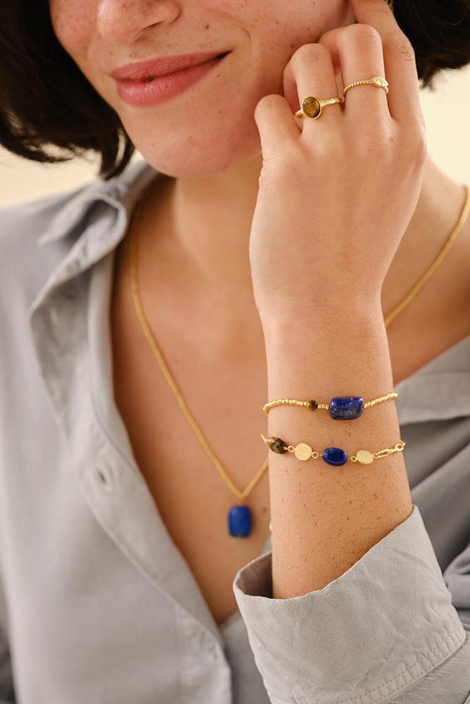 Woman wearing gold jewelry with blue stones on a neutral background