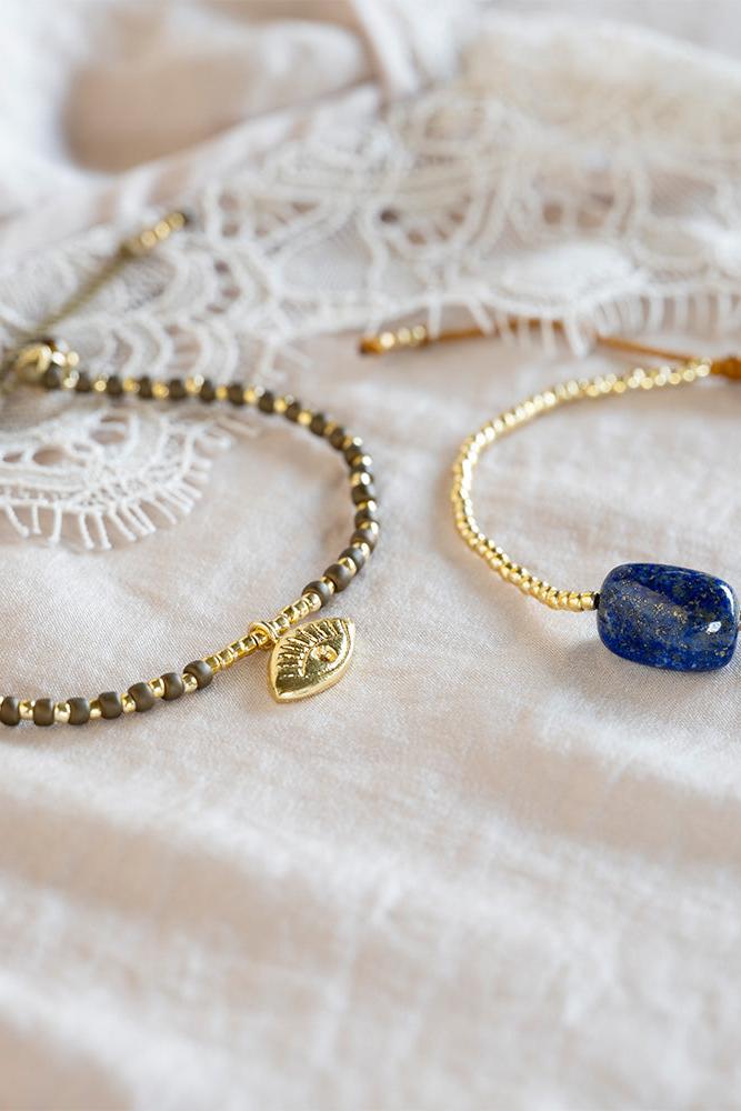 Two gold bracelets with an eye charm and a blue stone on a white lace background