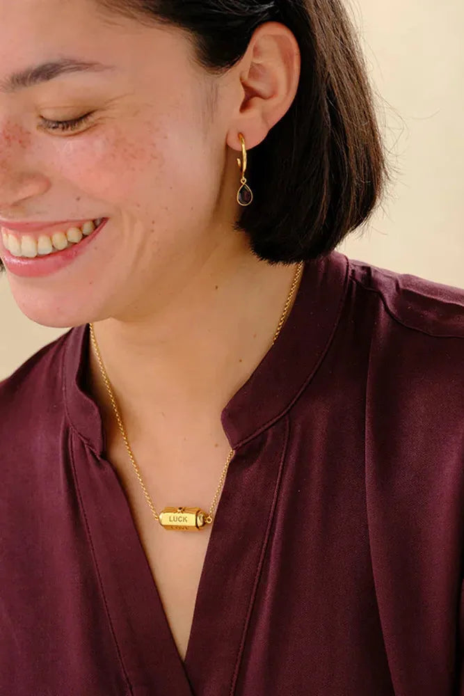 Woman wearing gold earrings and a necklace with a visible brand name.