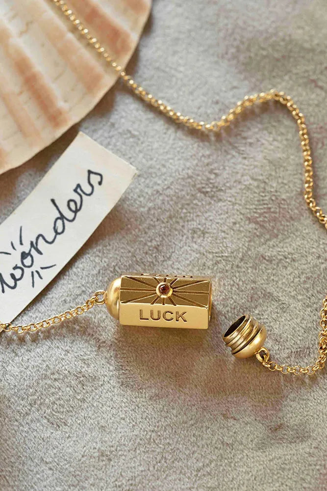 Gold necklace with a 'LUCK' pendant on a textured surface, featuring the brand 'wonders'.