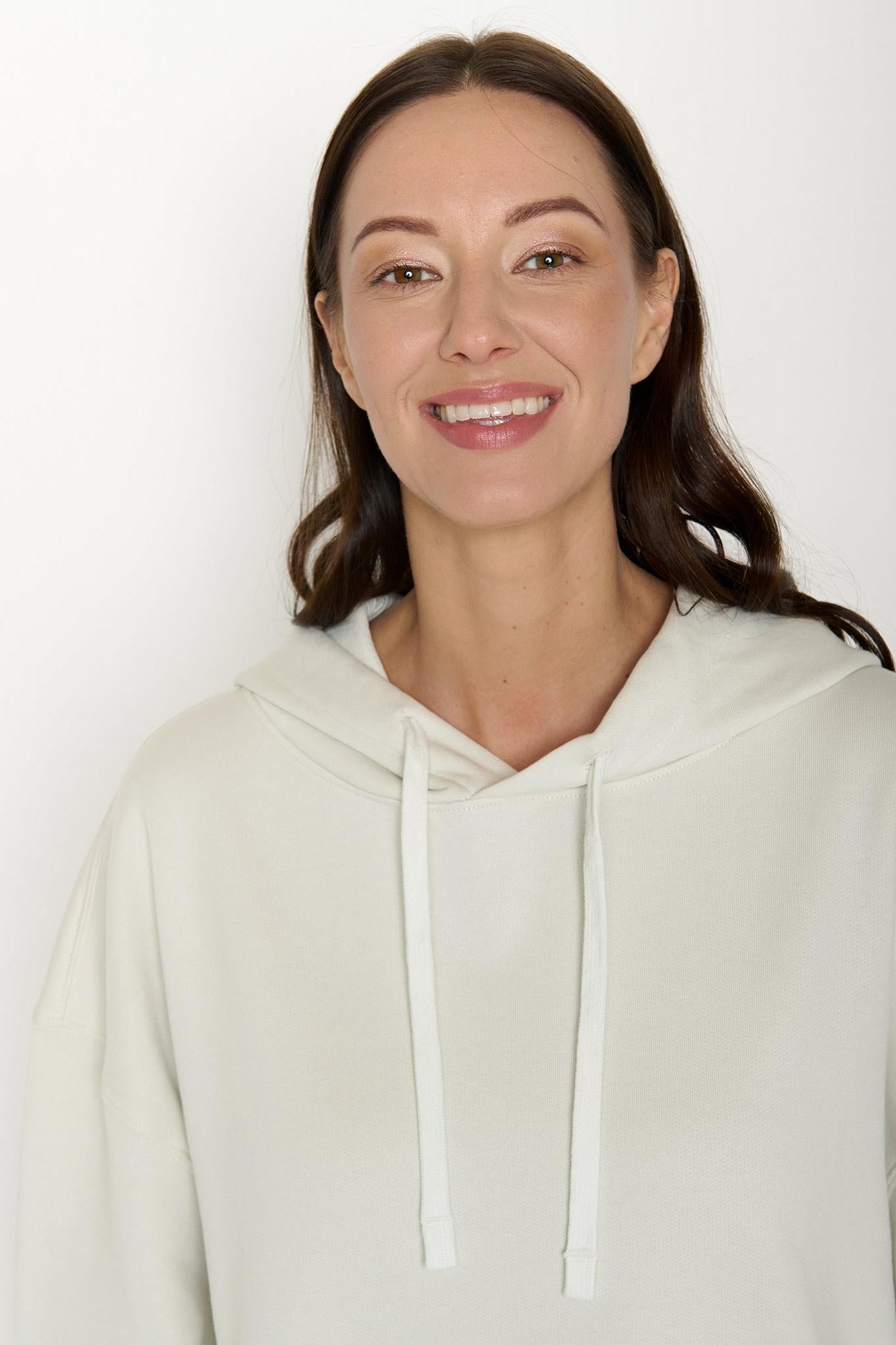 Woman wearing a white organic cotton hoodie against a plain background