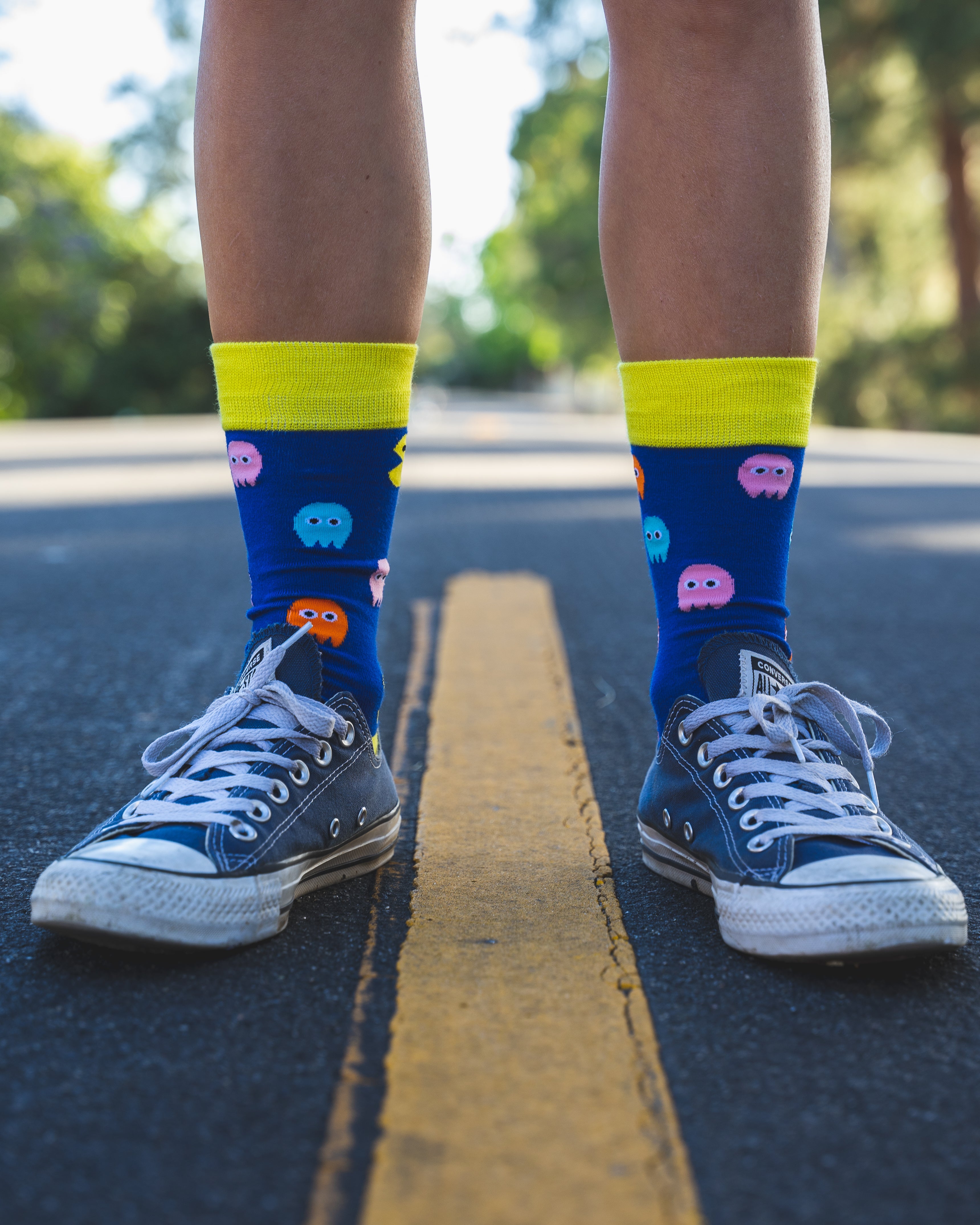 Person wearing blue socks with colorful designs and yellow accents, standing on a road.