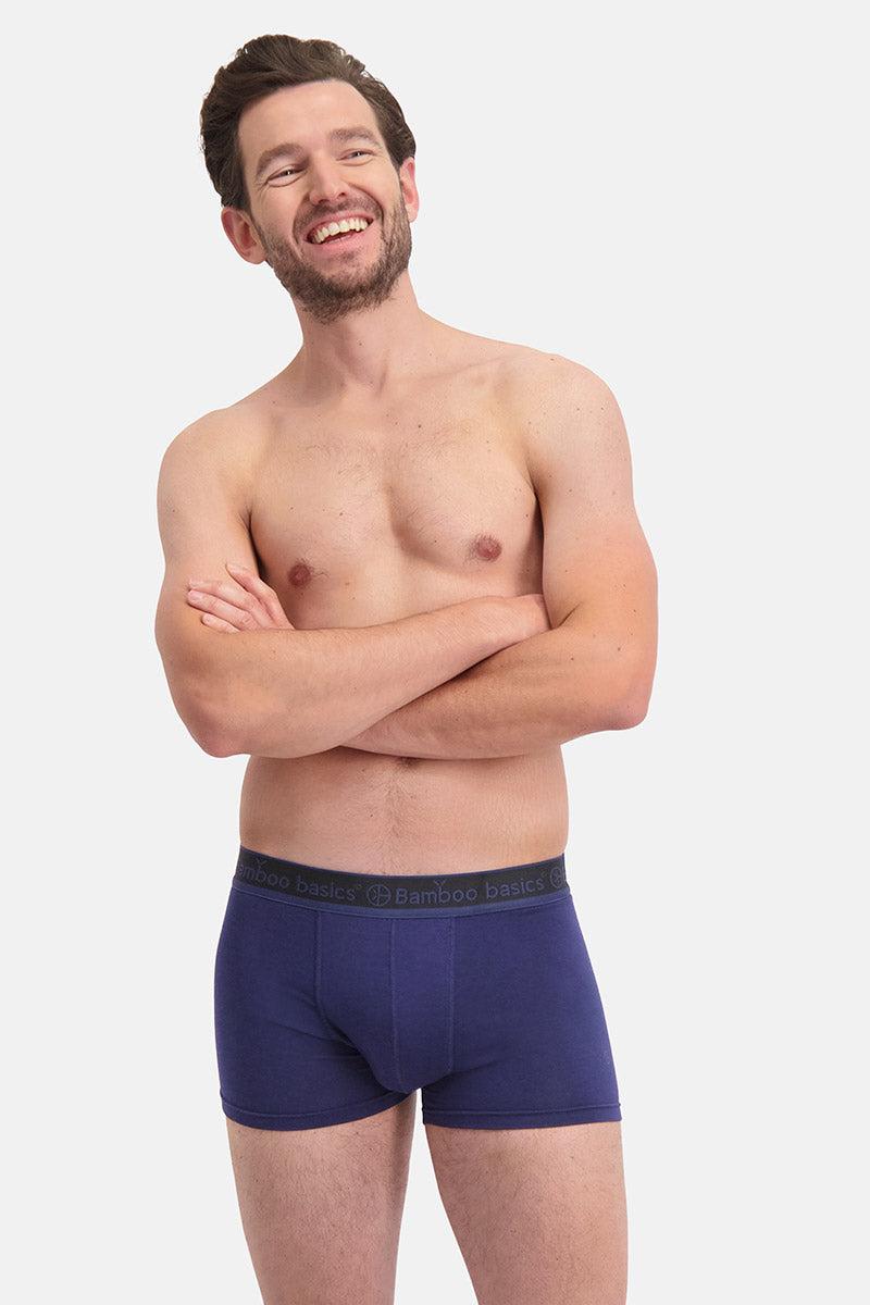Man wearing a pair of blue boxer briefs on a plain background