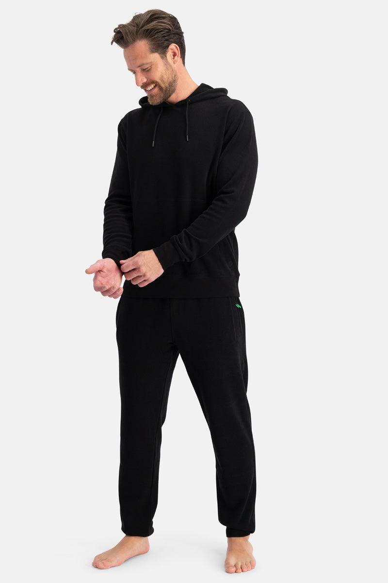 Man wearing a black organic cotton hoodie and pants on a white background