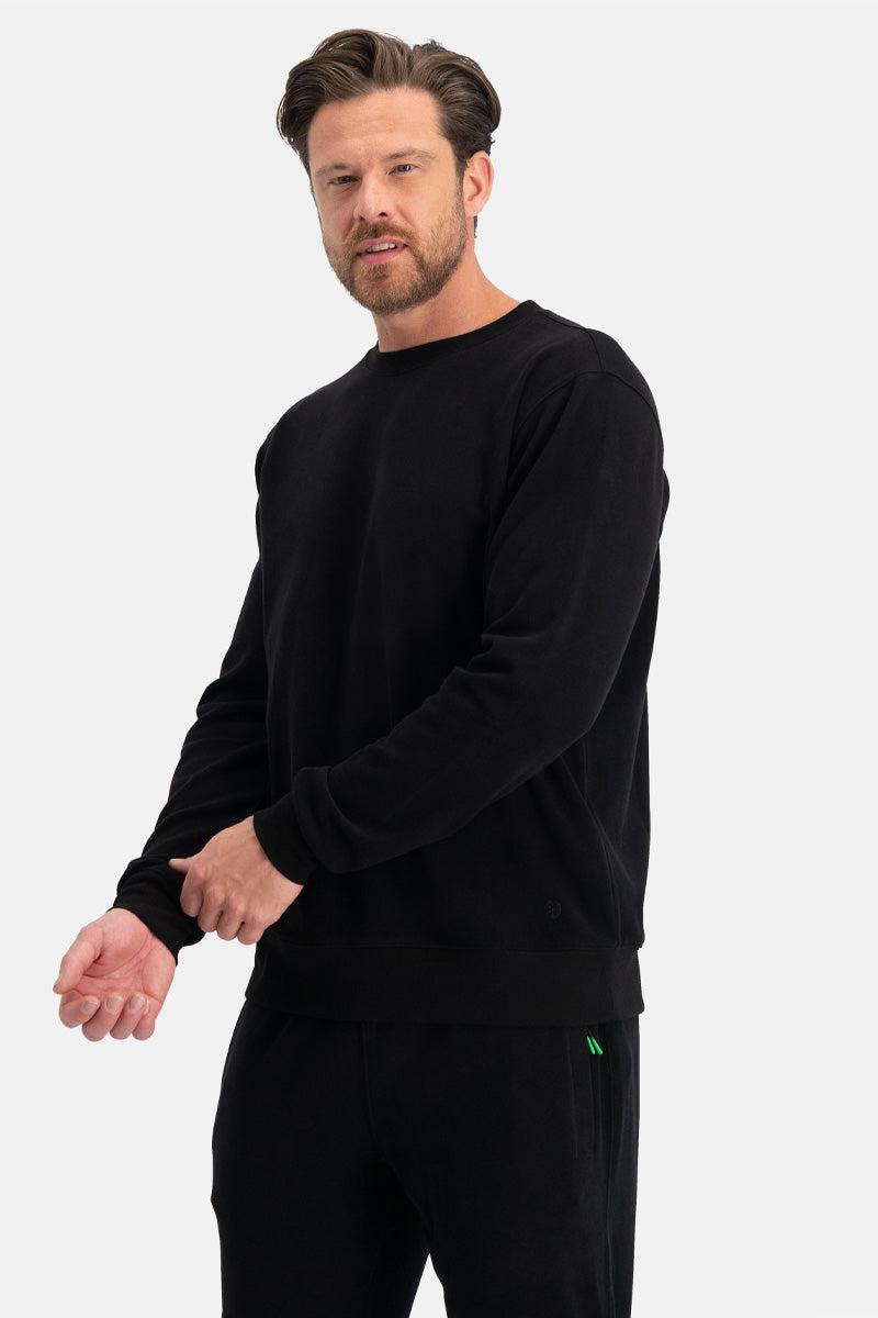 Man wearing a black long-sleeve sweatshirt and pants on a white background