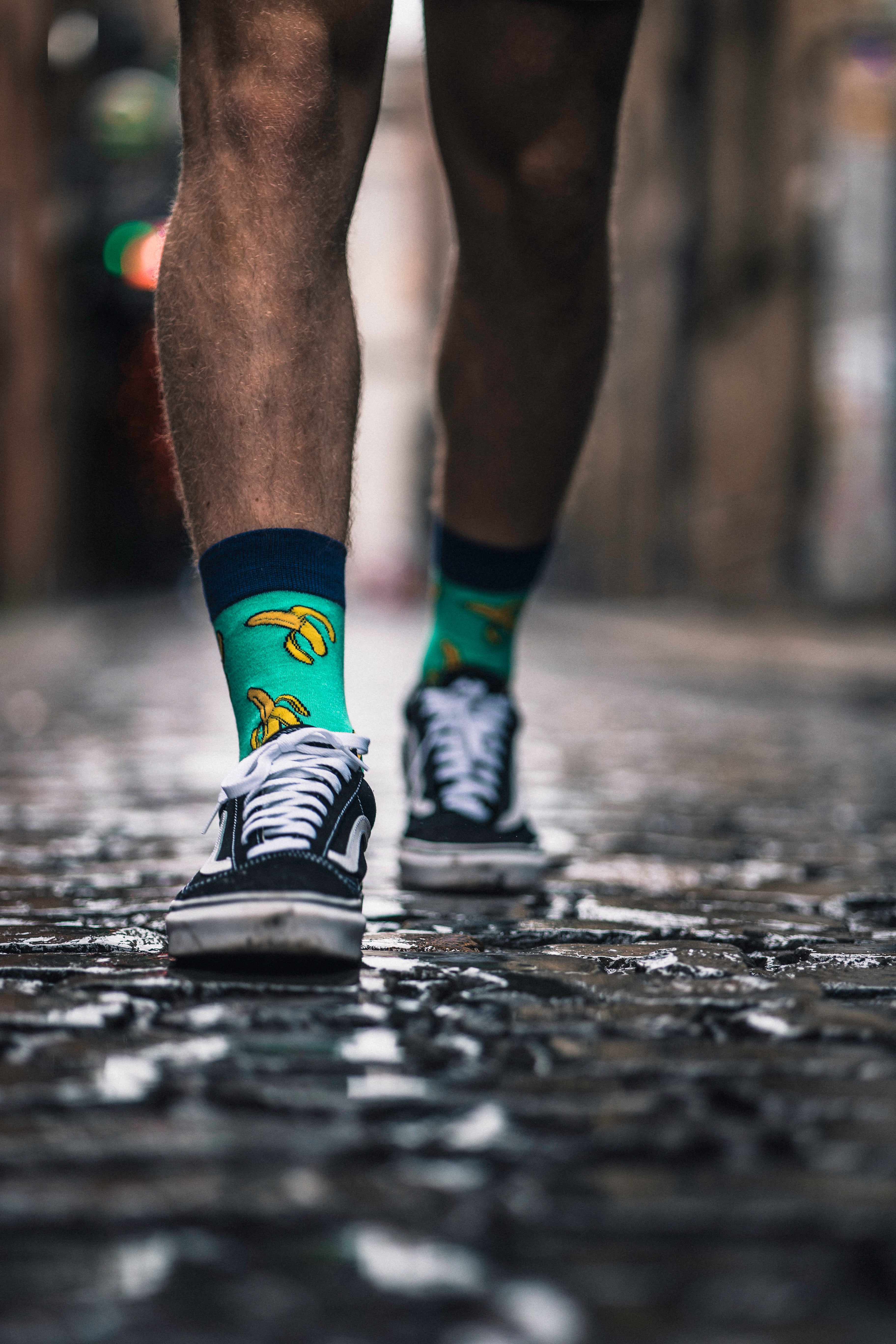 Close-up of legs wearing colorful socks and black sneakers on a cobblestone street.