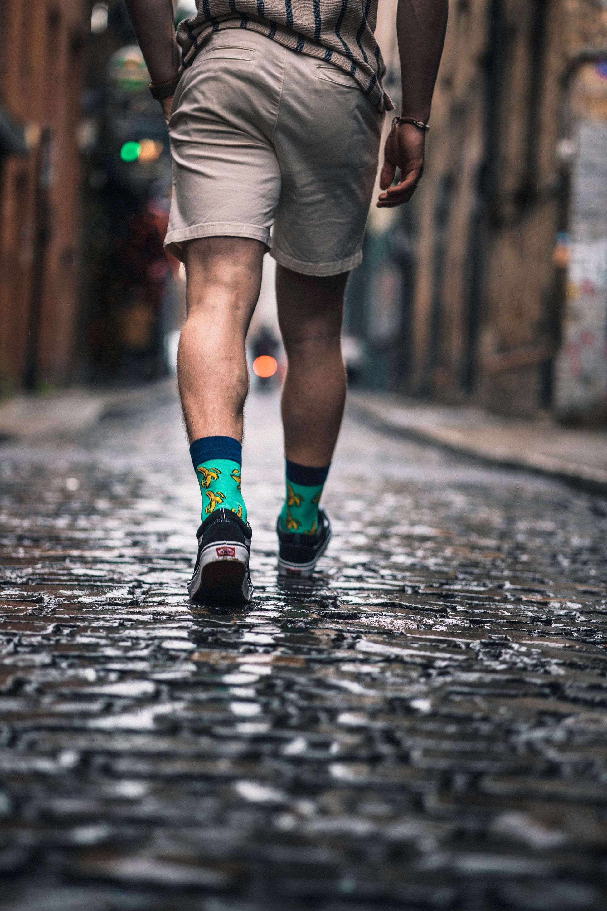 Person walking on a cobblestone street wearing shorts and colorful socks.