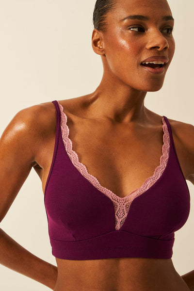 Woman wearing a purple bralette with lace trim against a beige background