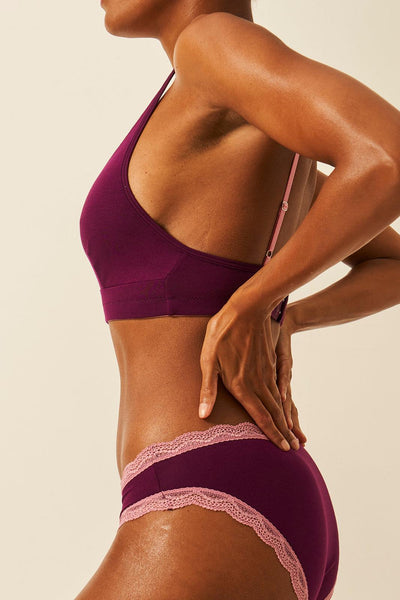 Person wearing a purple bra and brief set on a beige background