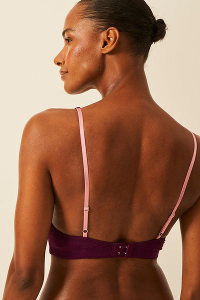 Woman wearing a purple tencel bra with pink straps on a beige background
