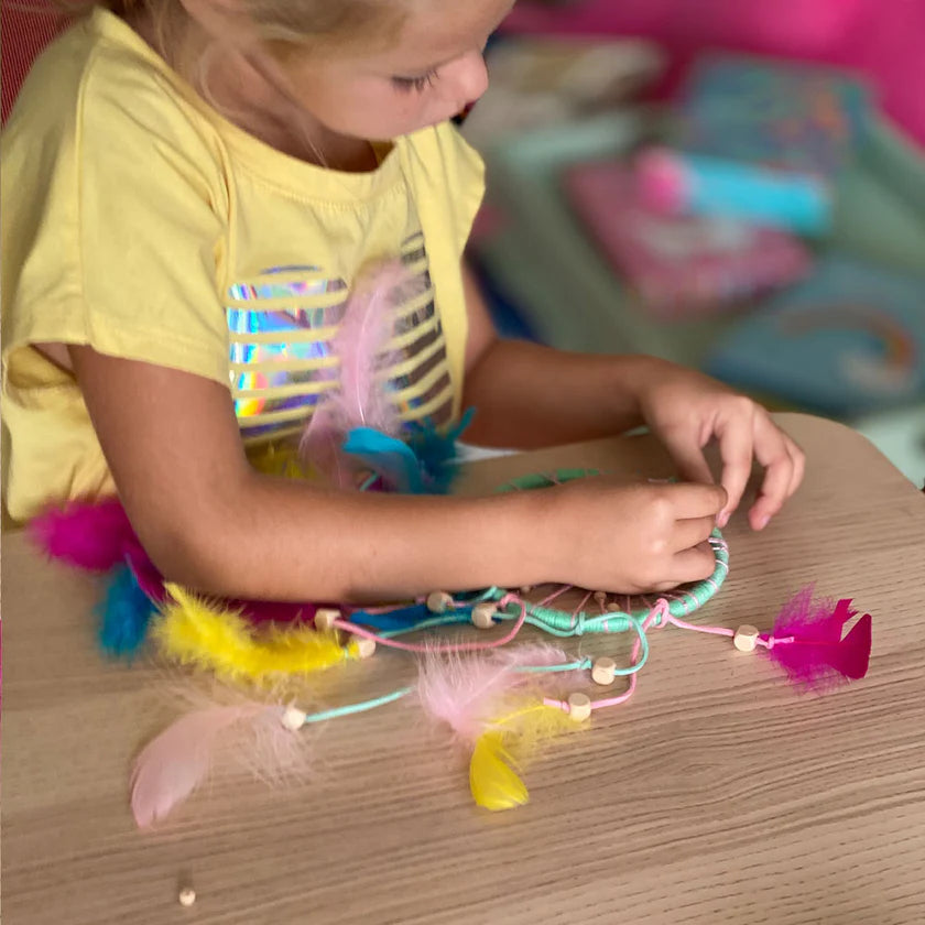 Child making a colorful craft with feathers and beads on a wooden table.