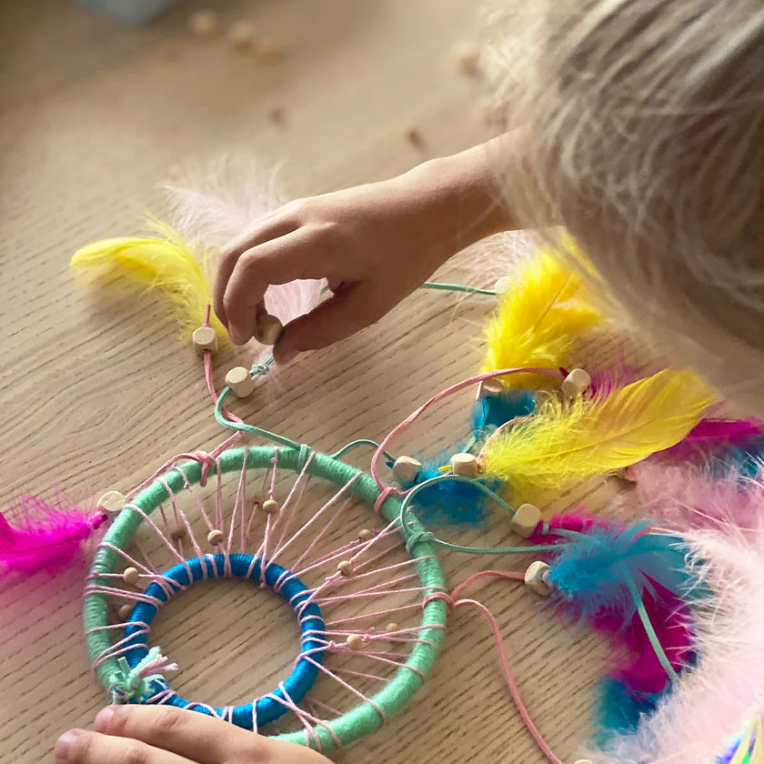Child's hand interacting with a colourful dreamcatcher on a wooden surface
