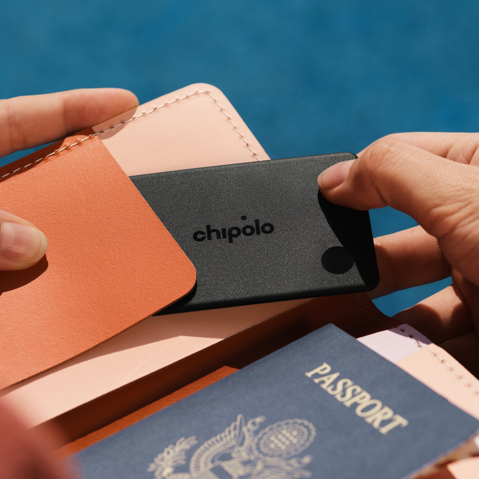 Person holding a Chipolo tracker with a passport and wallet against a blue background