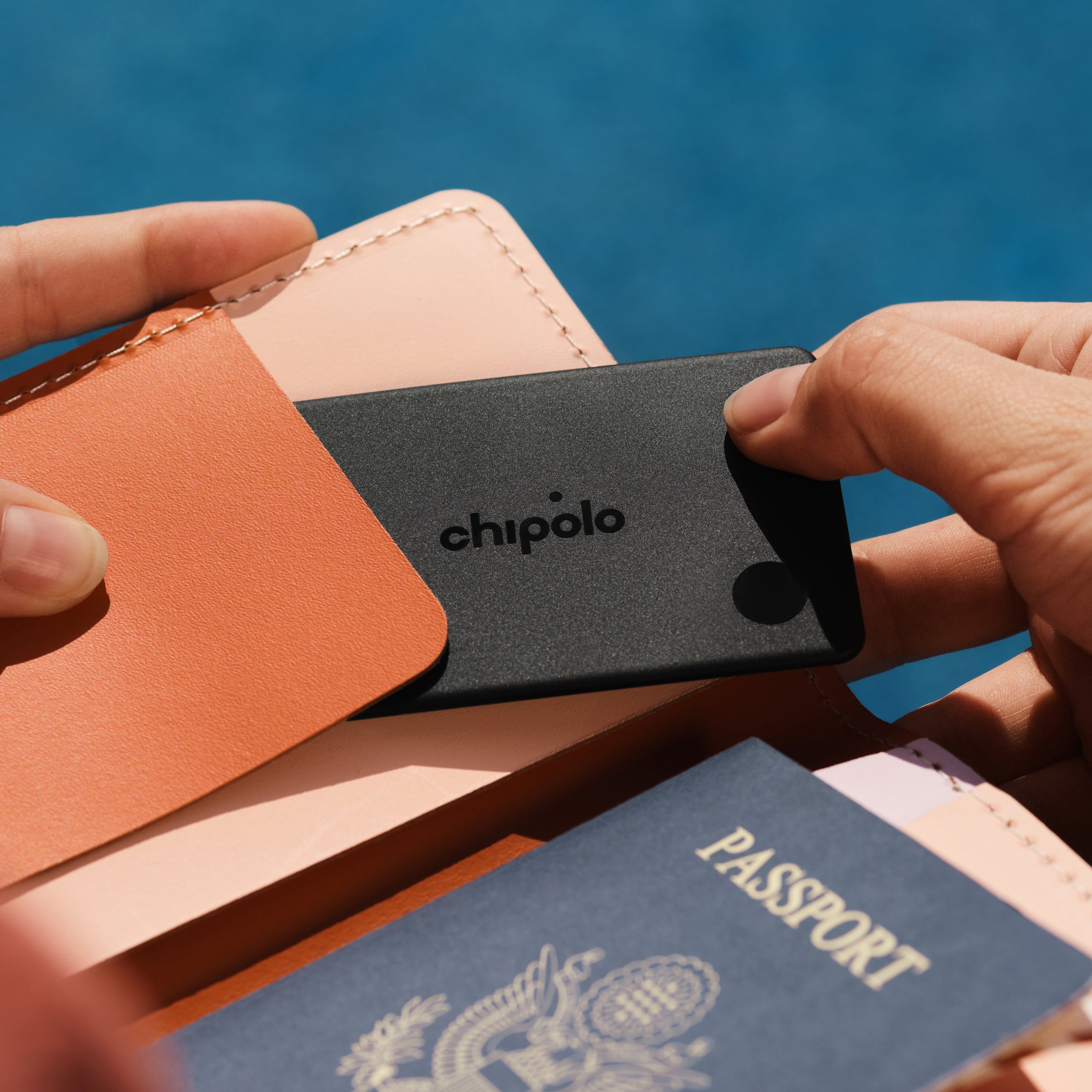 Person holding a Chipolo tracker with a passport and wallet against a blue background