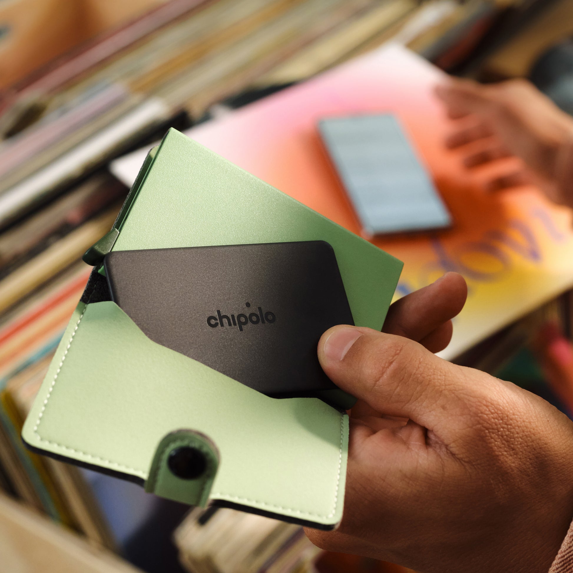 Hand holding a green and black cardholder with 'chipolo' branding, blurred background