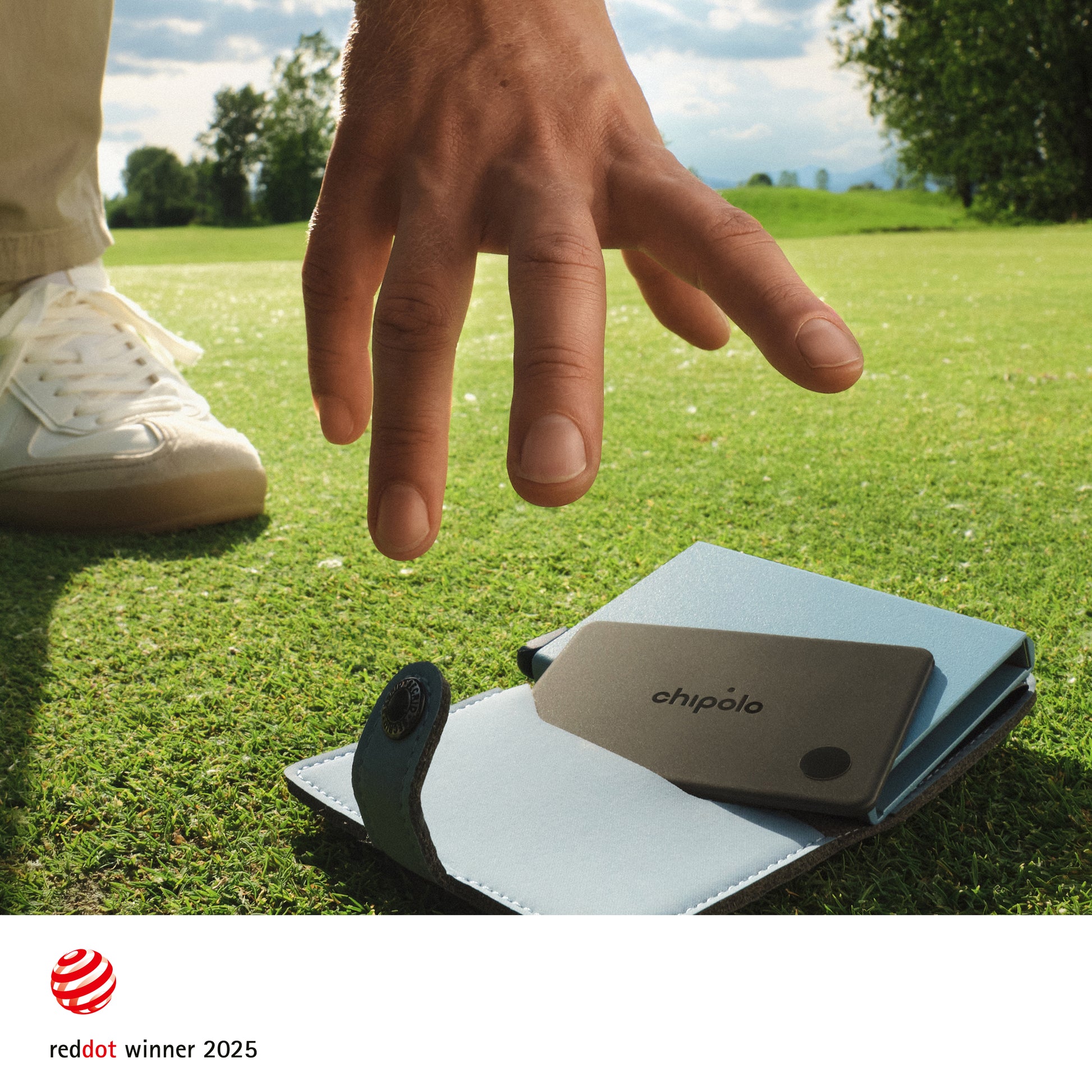 Hand reaching towards a small Chipolo device on grass with 'chipolo' branding
