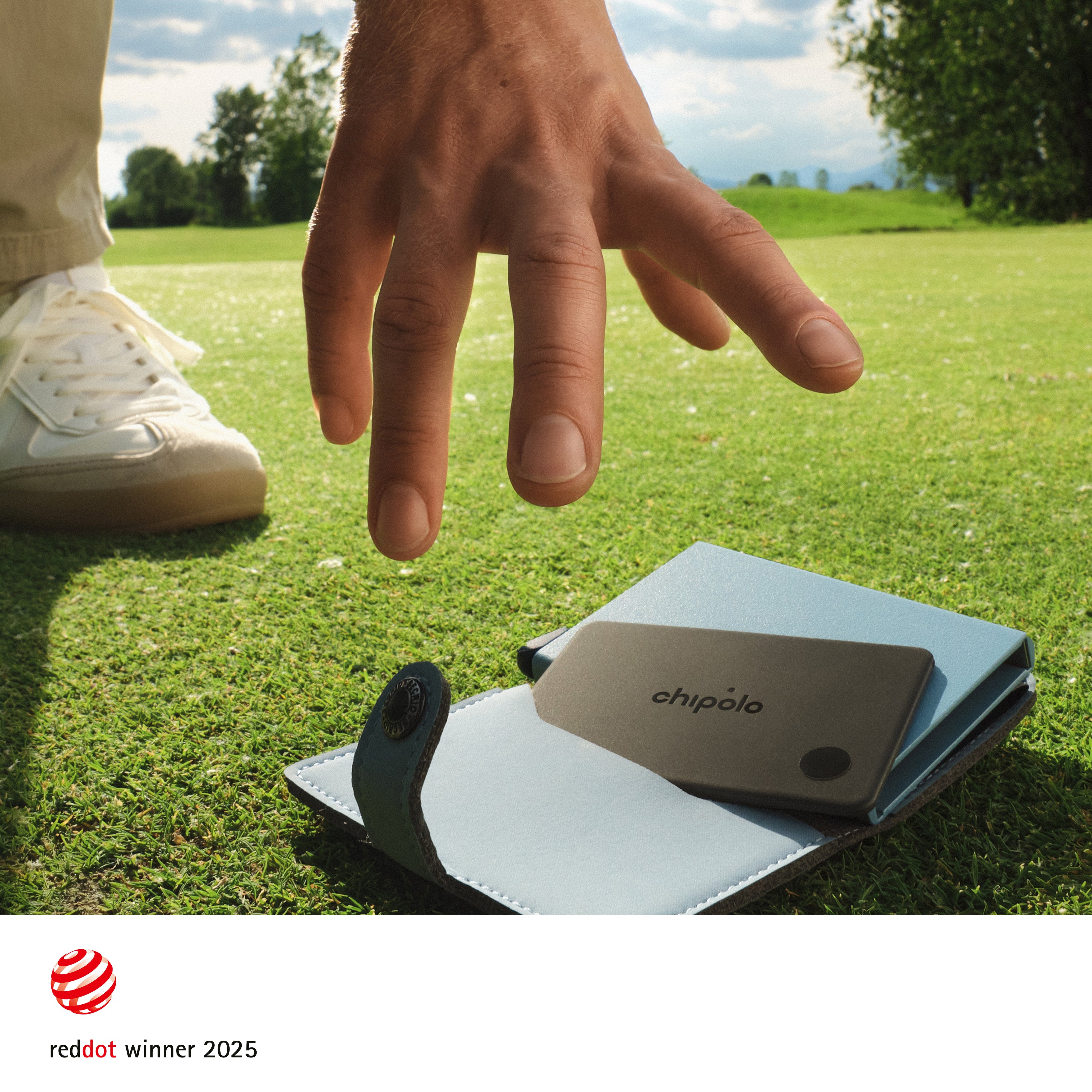 Hand reaching towards a small Chipolo device on grass with 'chipolo' branding