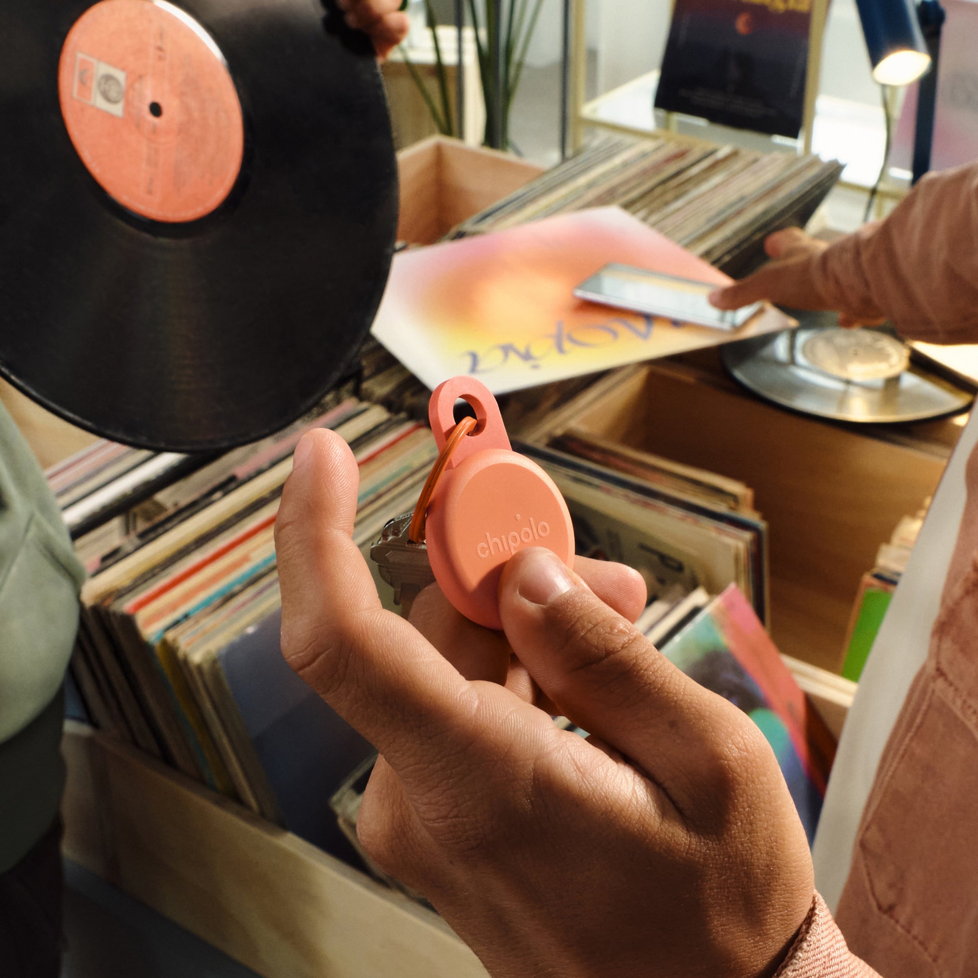 Person holding a pink 'Chipolo' product with vinyl records in the background