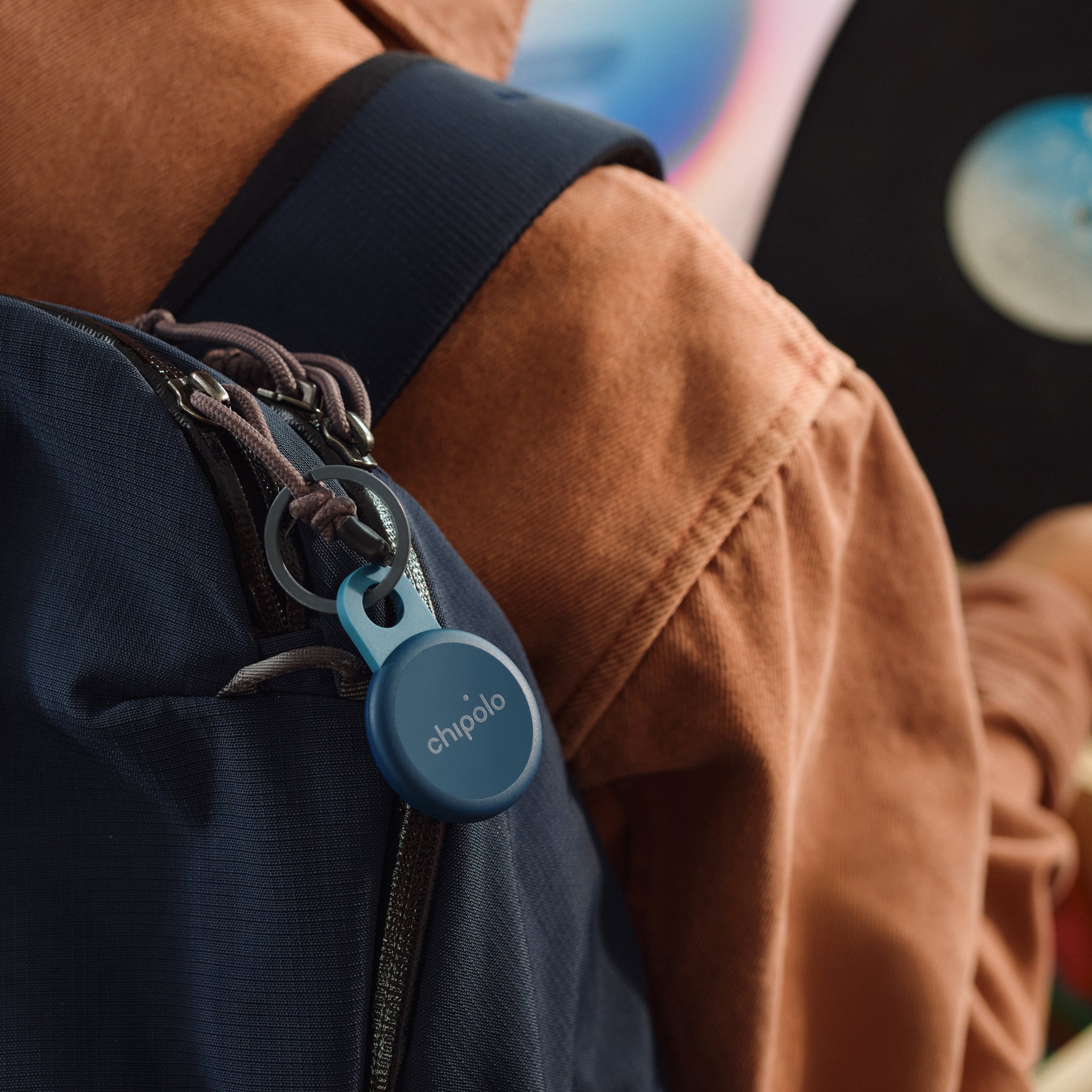 Blue Chipolo tracker on a keychain attached to a backpack with a blurred background