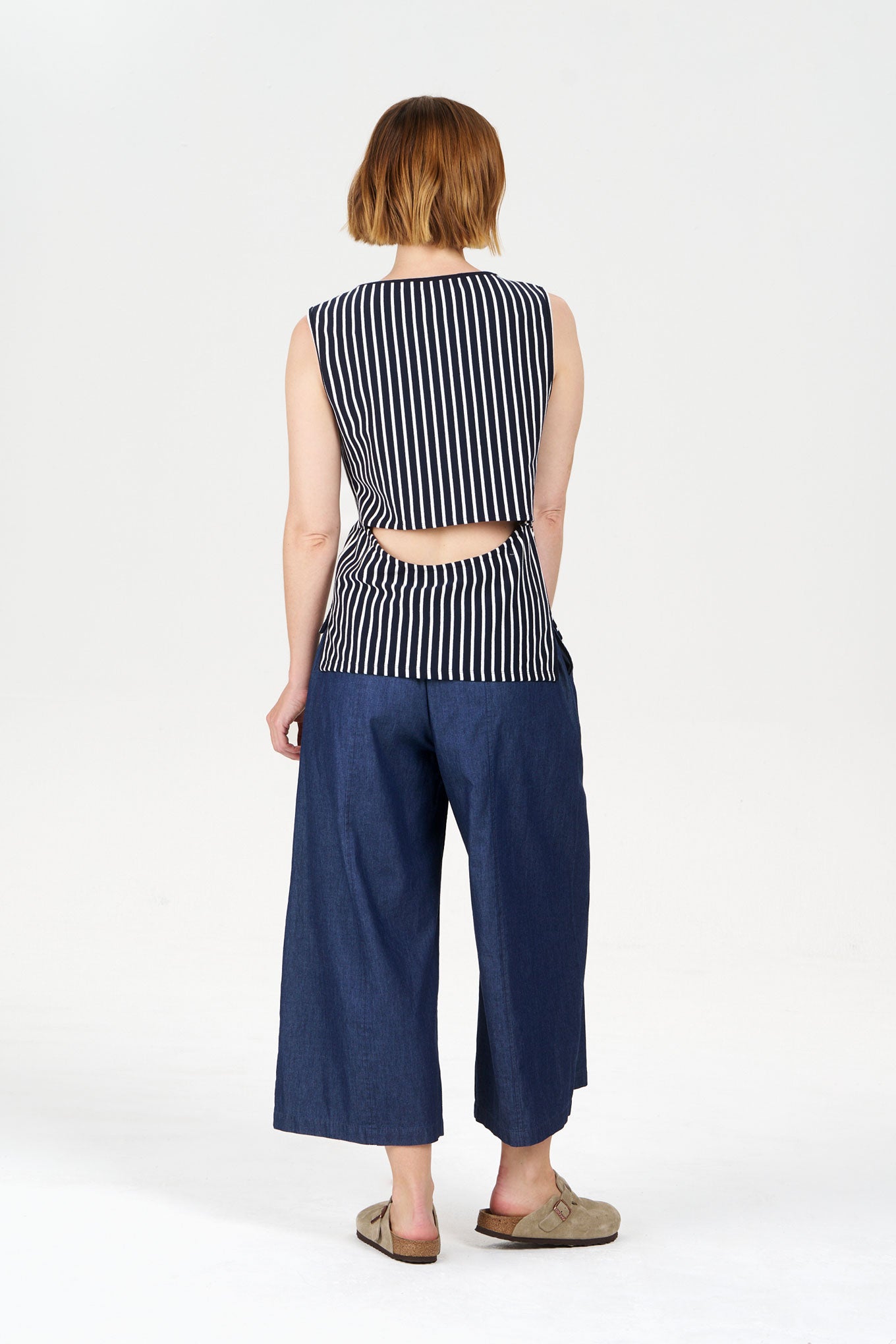 Woman wearing a navy and white striped sleeveless top and blue wide-leg pants on a white background