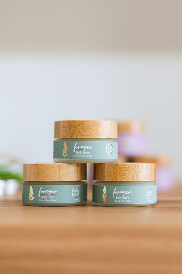 Three small jars with green Forager labels and wooden lids on a wooden surface.