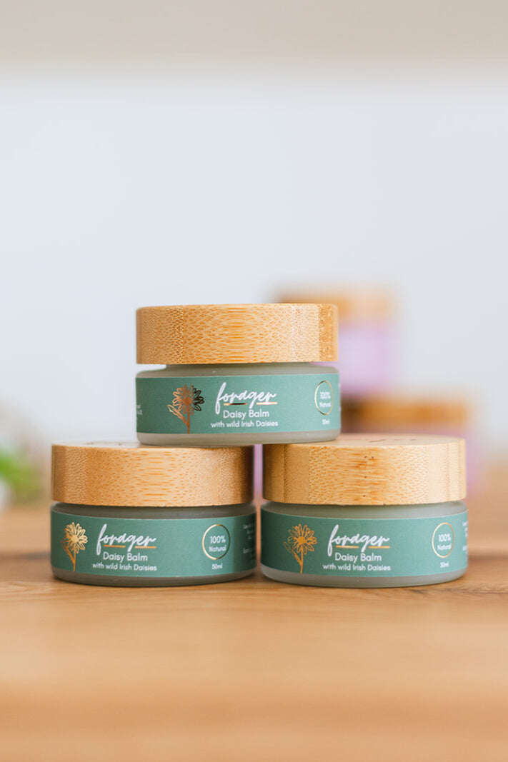 Three jars of 'Forager' balm stacked on a wooden surface with a blurred background