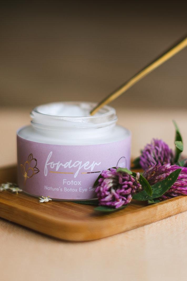 Purple jar of Forager eye serum on a wooden board with flowers