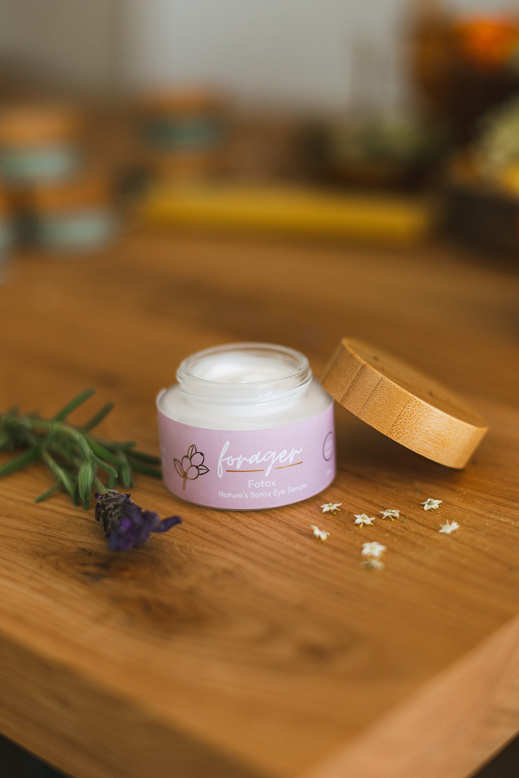 Pink jar of cream with wooden lid on a wooden surface with flowers and blurred background