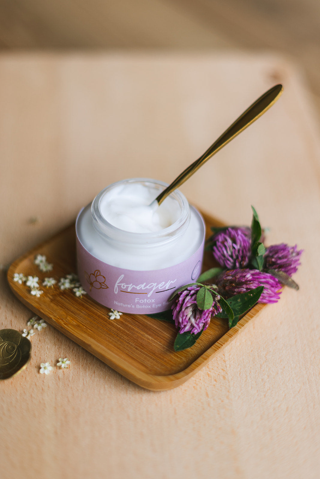 Jar of cream with a spoon on a wooden tray surrounded by flowers