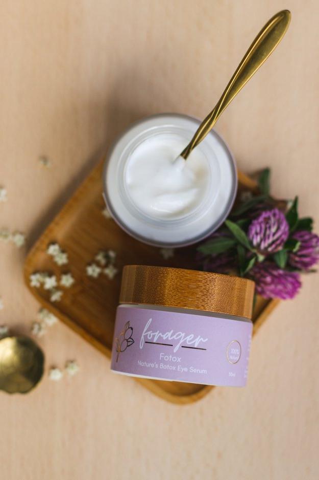 Two jars of cream with a wooden lid on a beige surface, surrounded by flowers.