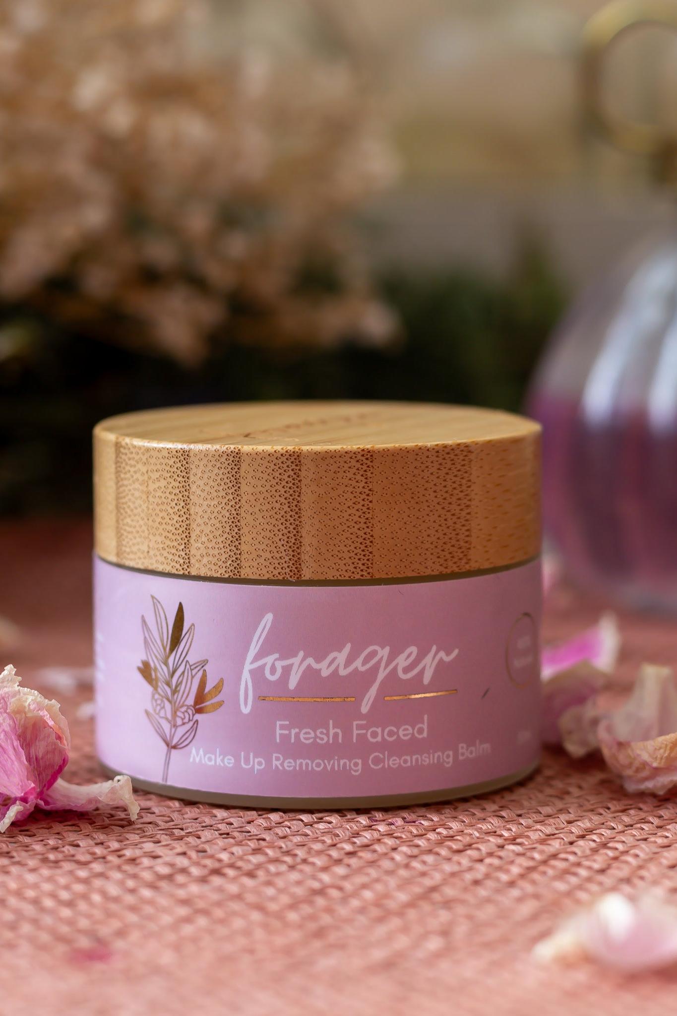Pink jar with wooden lid labeled 'forager' on a pink surface with blurred background