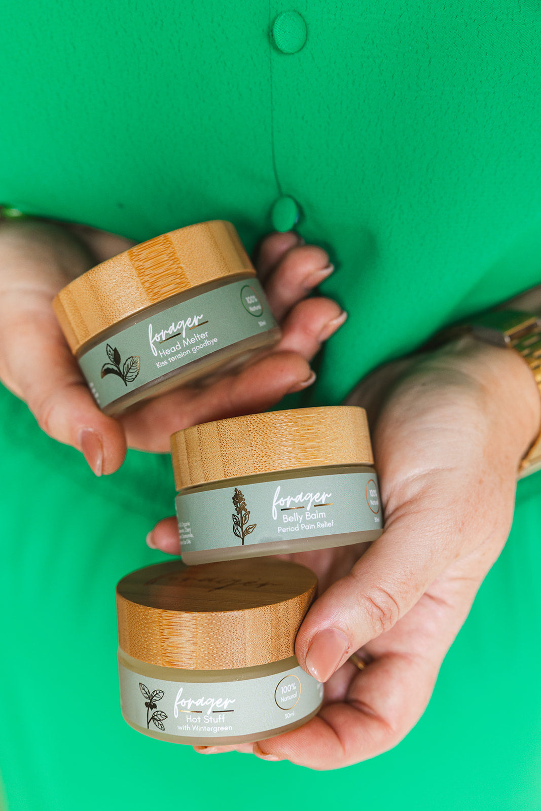 Three jars of facial cream held by hands against a green background