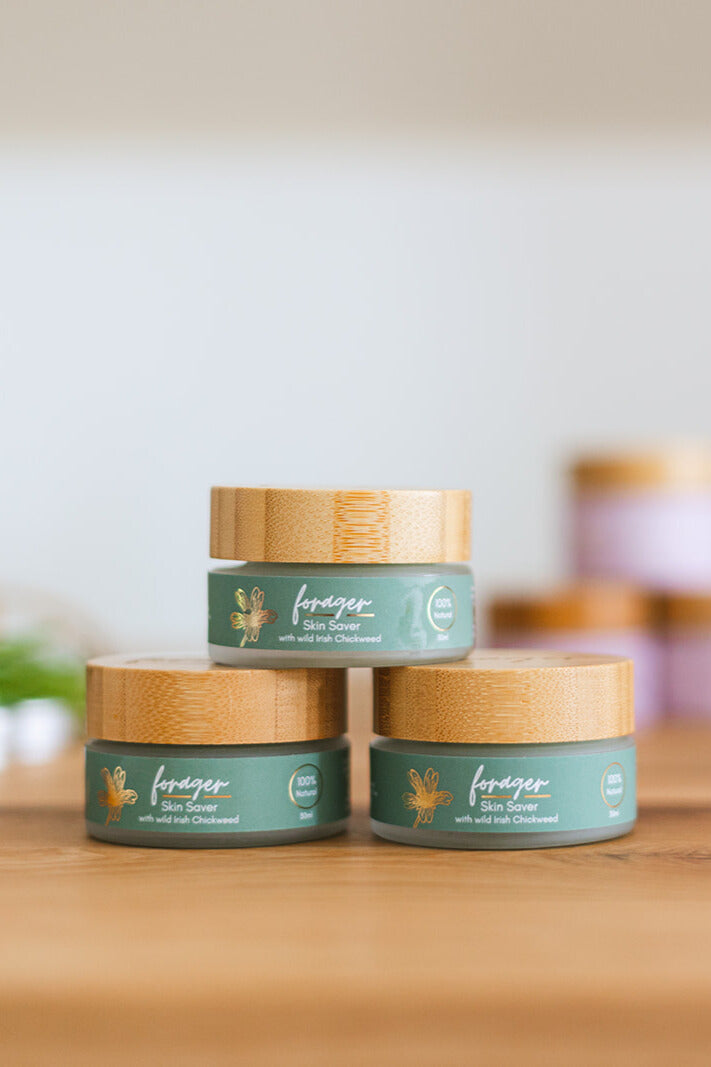 Three jars of Forager skin balm on a wooden surface with a blurred background