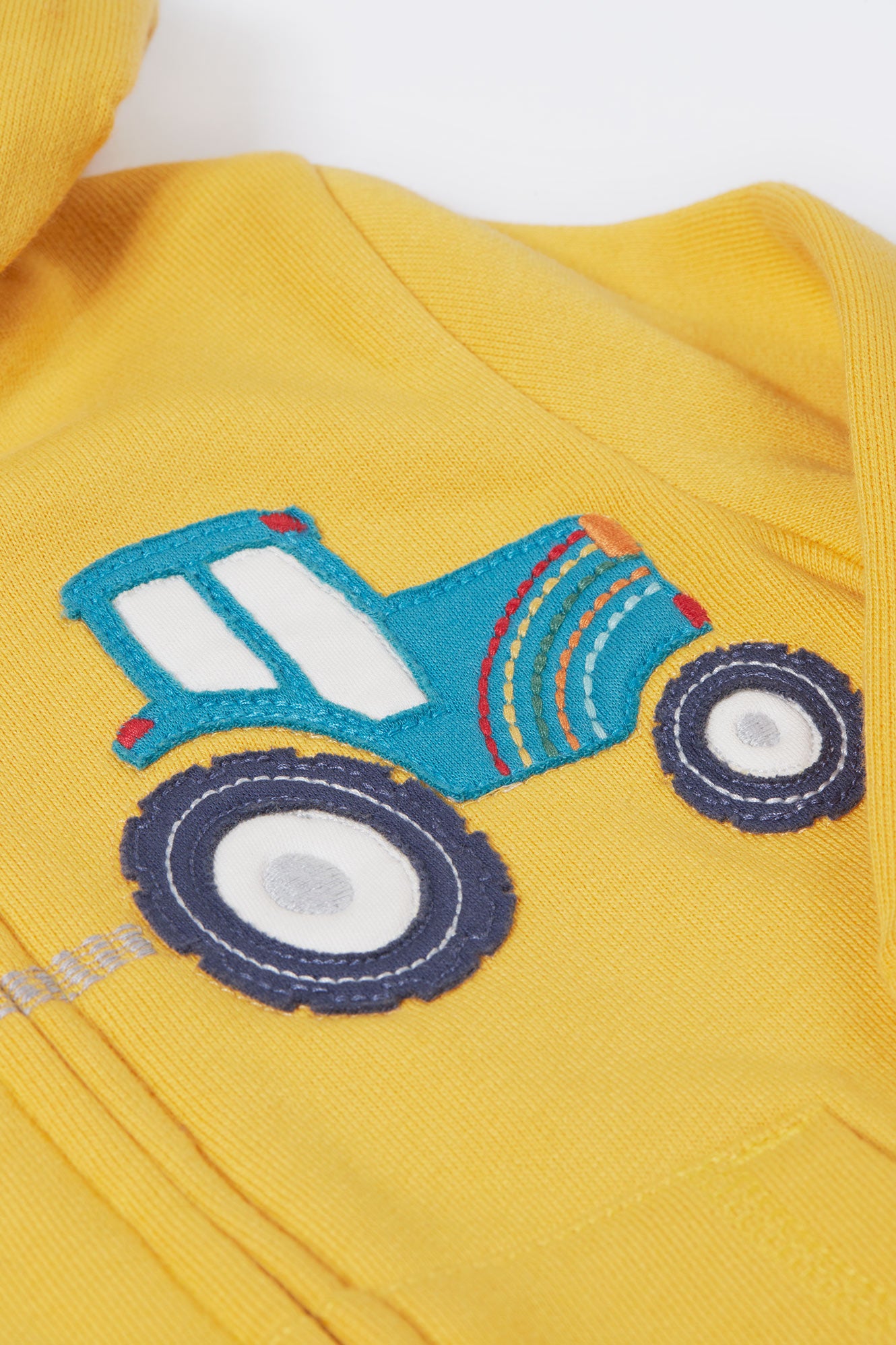 Close up of tractor applique detail on yellow organic cotton hoodie for kids