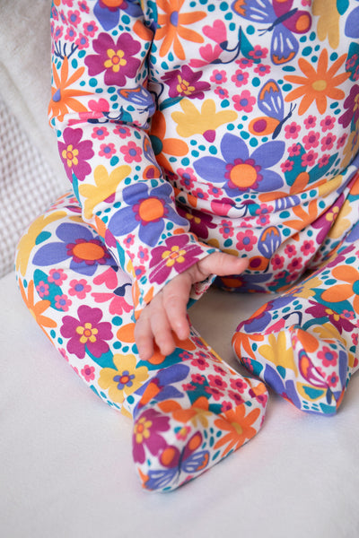 Baby wearing a colourful organic cotton babygrow sitting on a white surface.