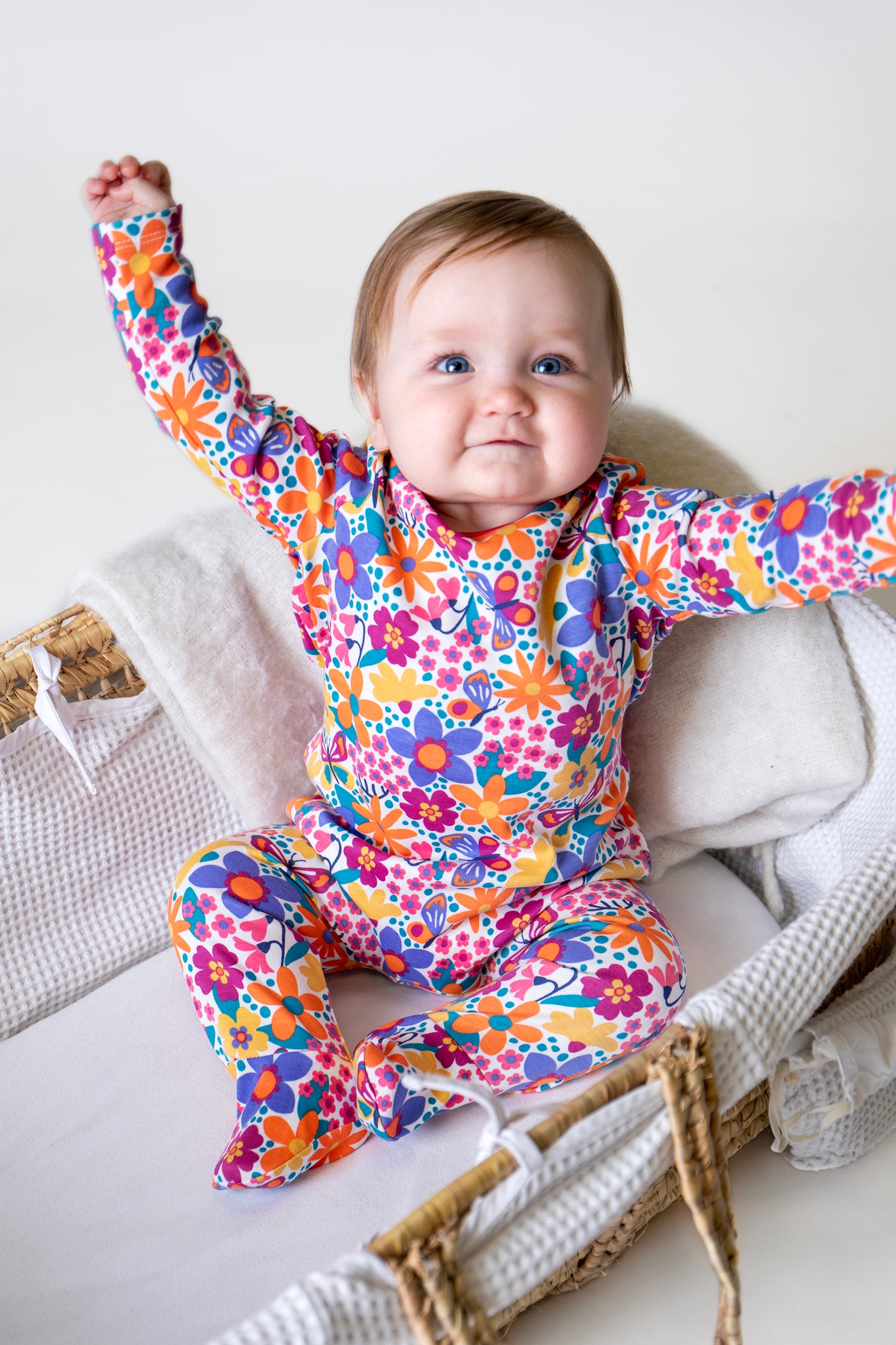 Baby wearing a colorful Frugi floral onesie sitting on a white surface.
