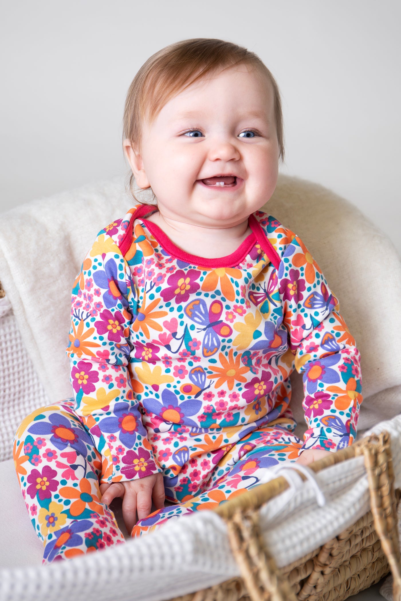 Baby wearing Frugi floral organic cotton babygrow sitting on a white surface.