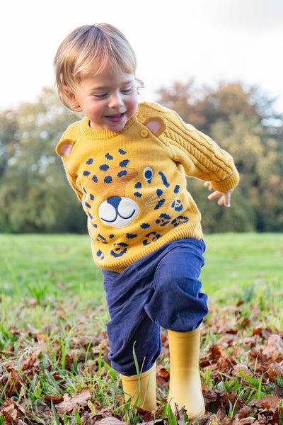 Child wearing a yellow sweater with a cartoon design, blue organic cotton pants, and yellow boots running in a field.