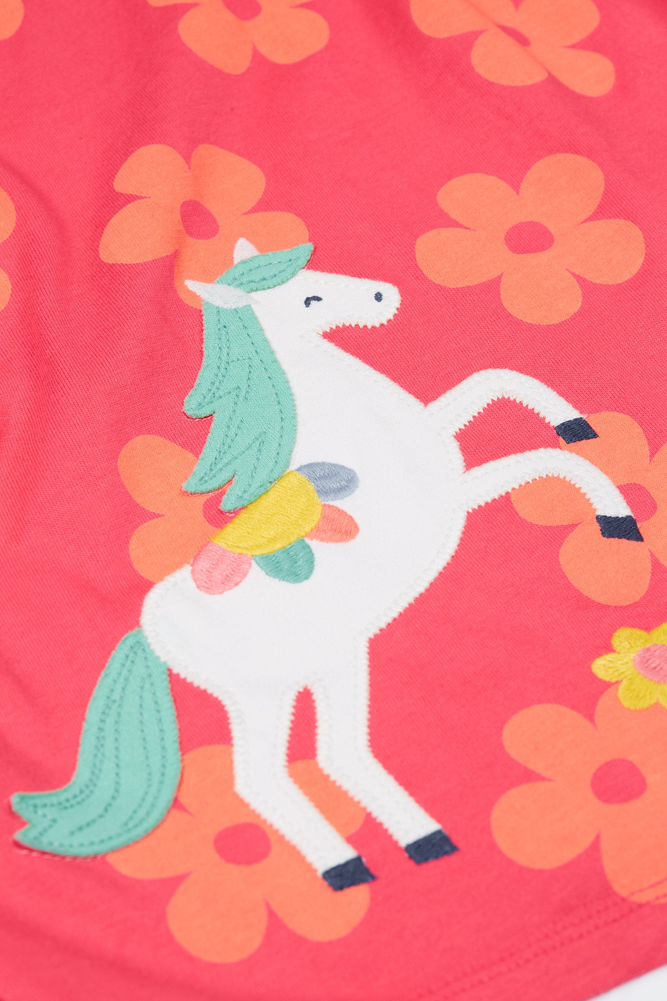 Detailed view of the white horse applique on the Frugi Little Lola Dress, showcasing its coloured mane and tail against the floral pattern.